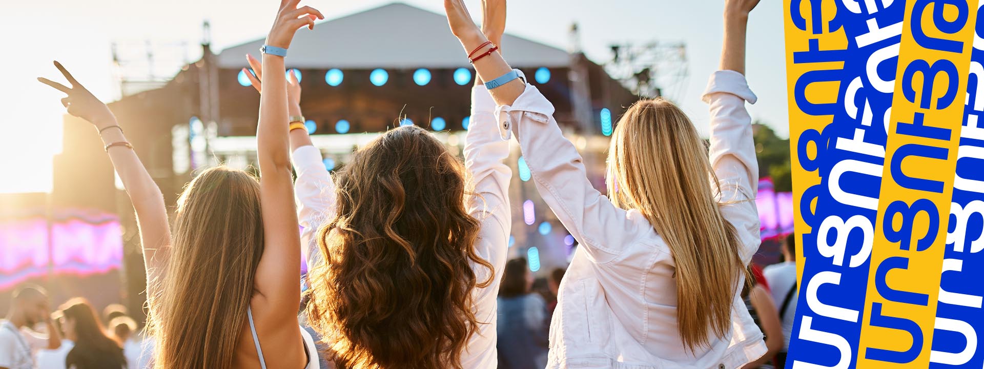 Three people with raised arms enjoy a music festival near a stage.