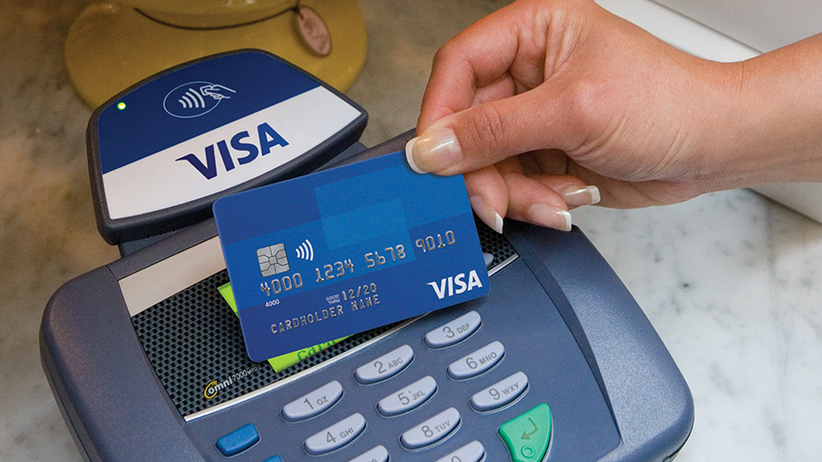 A hand holding a Visa card over a contactless POS system.