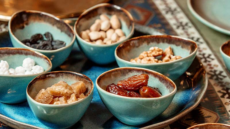 A close-up of several blue bowls filled with assorted dried fruits, nuts, and candies arranged on a blue tray.